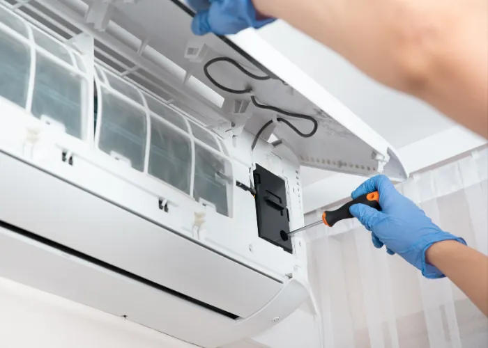 Gloved technician servicing an open aircon indoor unit with the filters lifted